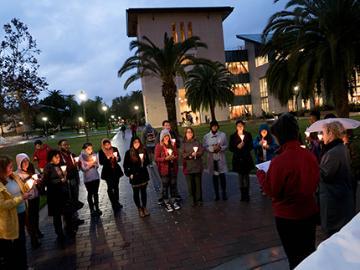A group of people holding candles at night in a plaza.