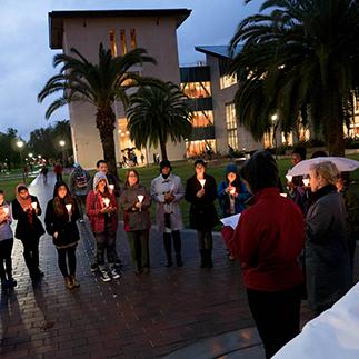 A group of people holding lit candles in an outdoor gathering at dusk.