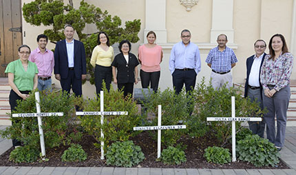 Group of nine people standing behind white crosses in a garden.
