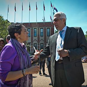 Two people talking outside, with flags and building visible in the background.