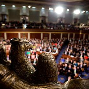 Audience in a large hall viewed from behind a bronze statue.