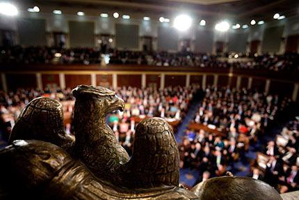 A large audience filling an amphitheater under bright ceiling lights.
