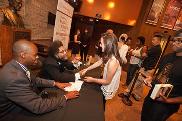 People at an event, signing documents and interacting at a table.