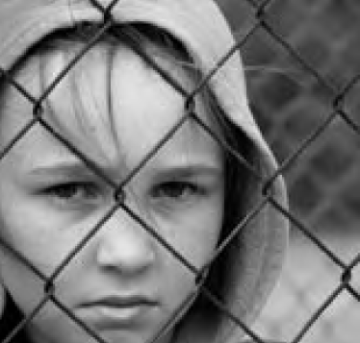 Black-and-white image of a person behind a chain-link fence.