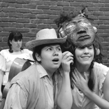 People posing with theatrical expressions and a lion mask in front of a brick wall. image link to story