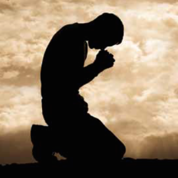 Silhouette of a person kneeling in prayer under a cloudy sky.