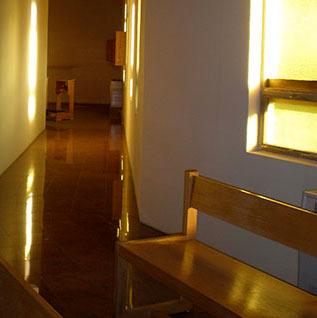 Dimly lit hallway of a church with wooden bench and window.