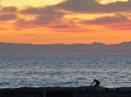 A surfer on the ocean at sunset with colorful sky.