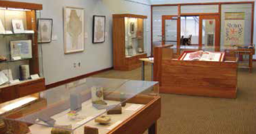 Museum exhibit room with display cases showcasing various artifacts and framed pictures on the walls.