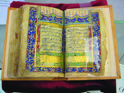 Illuminated Koran with intricate borders displayed on a stand.