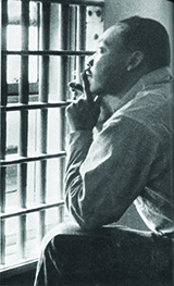 A person seated, looking through barred windows, with hand resting on chin.