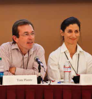 Two individuals sitting behind a conference table with microphones and name tags.
