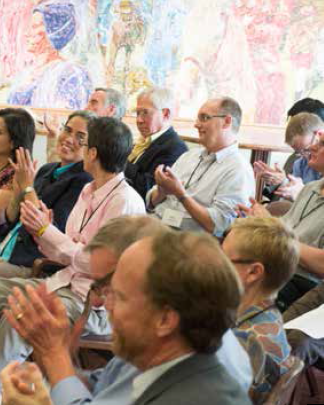 People seated and applauding in a room with colorful artwork.