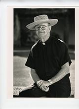 A person seated outdoors wearing a hat and dark clothing.