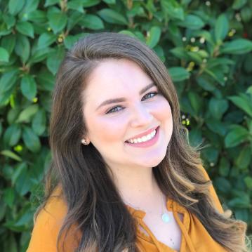 Smiling woman in front of greenery.