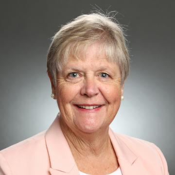 A person smiling in formal attire against a gray background.