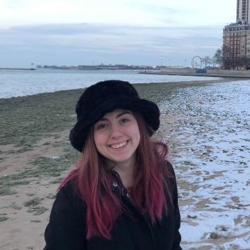 A person standing on a snowy beach, smiling, wearing a black hat and coat.