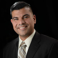 A man in a suit and tie smiling in front of a black background.