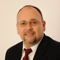A man in a suit and tie, wearing glasses.