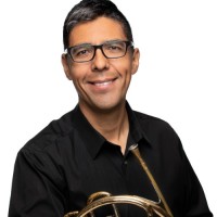 A smiling person holding a French horn.