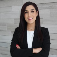 A person in a suit stands against a wood-paneled wall.
