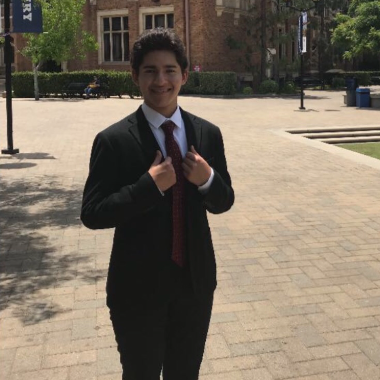 A person in a suit standing outdoors adjusting their tie. 