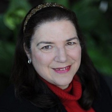 A woman wearing a red scarf, smiles in front of greenery.