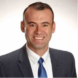 A person in a suit and tie smiling against a white background.