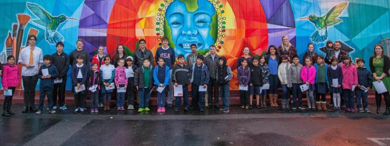 Group of people posing in front of a colorful mural with the text “Thriving Neighbors Initiative”. image link to story