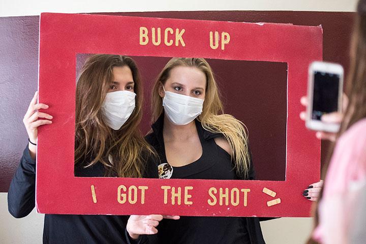 Two people wearing masks holding a red frame with 