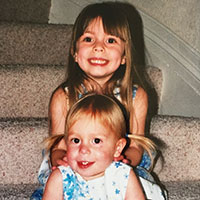 Two smiling children sitting on carpeted stairs.