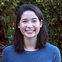 A woman smiling in front of a foliage background.