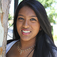 A smiling woman standing outside near a tree.