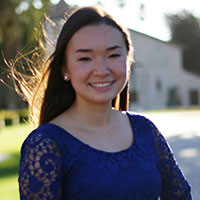 A woman in a blue lace dress smiling outdoors.