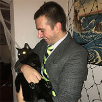 A person in a suit holding a black cat.