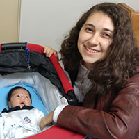 Woman smiling and sitting next to a baby in a stroller.