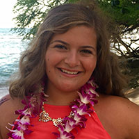 A smiling person wearing a pink lei at the beach.