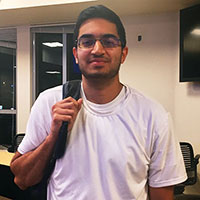A person named Ahmed holding a backpack strap and smiling.