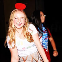 Two people at an event, one smiling with a red bow headband.