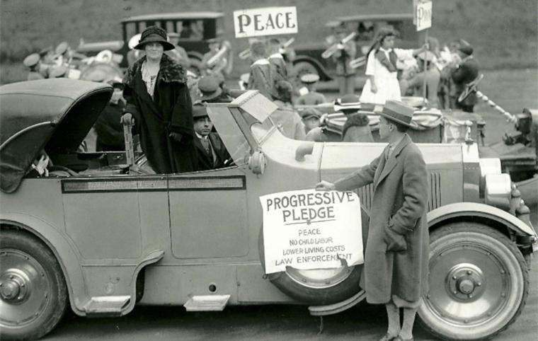 Black and white photo of Belle La Follette standing beside a decorated car. image link to story