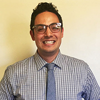 A person wearing glasses, a striped shirt, and a tie, smiling.