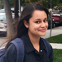 Person outdoors smiling with a backpack, trees, and parked cars in the background.