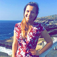 A person with a floral dress stands by a seaside.