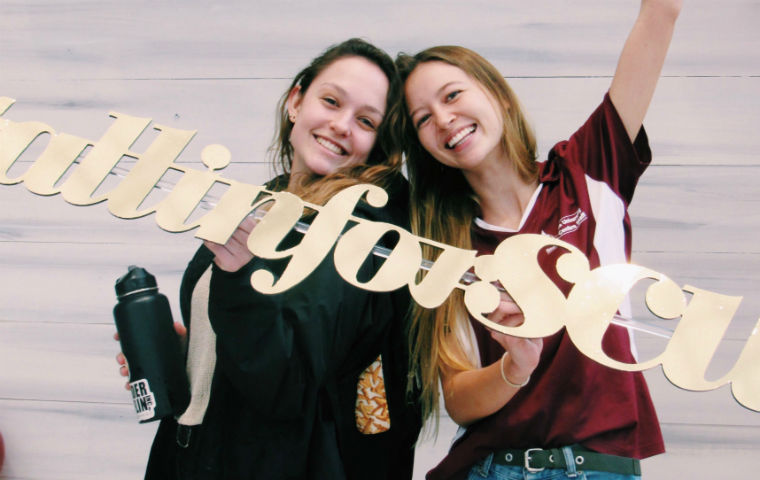 Two smiling female students holding All In For SCU sign