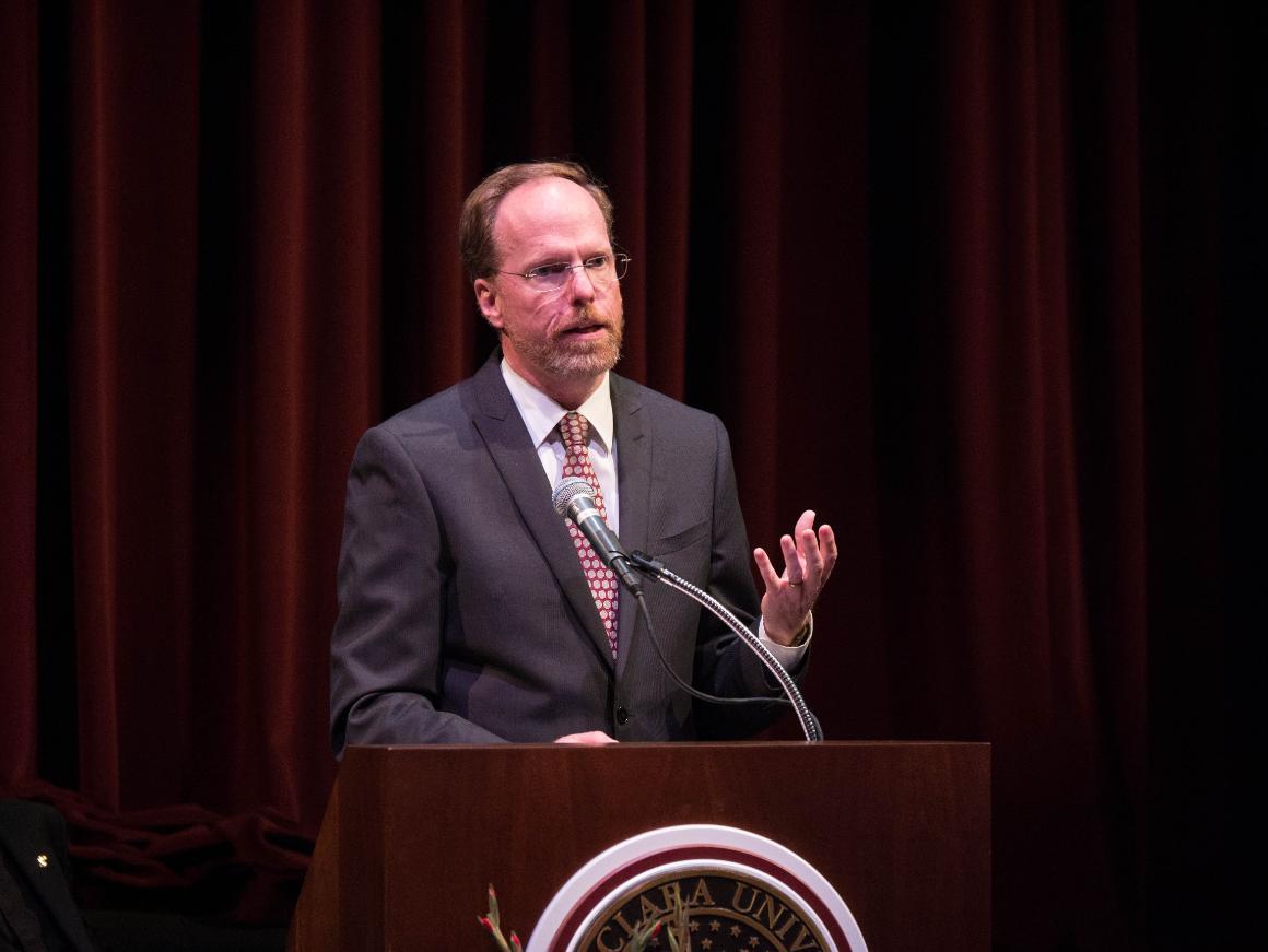 Man giving a speech behind a podium with a university seal.