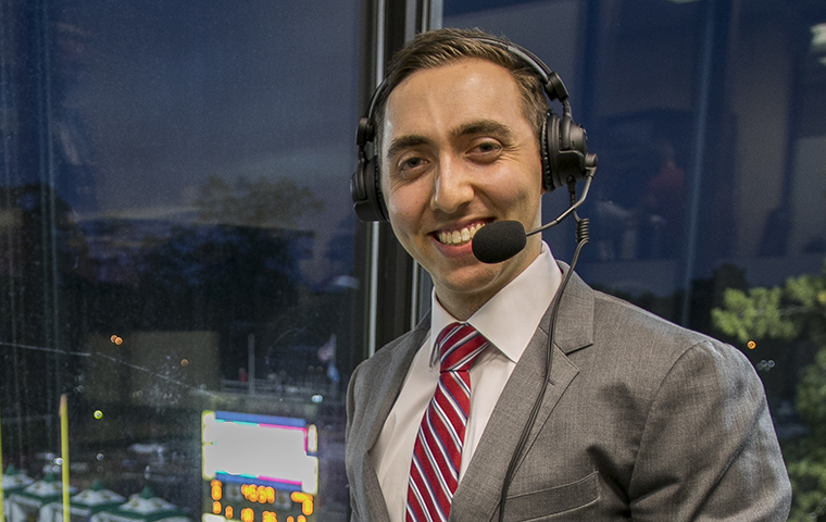 Announcer Jack Benjamin stands in press box at Nicholls State with microphone headset.