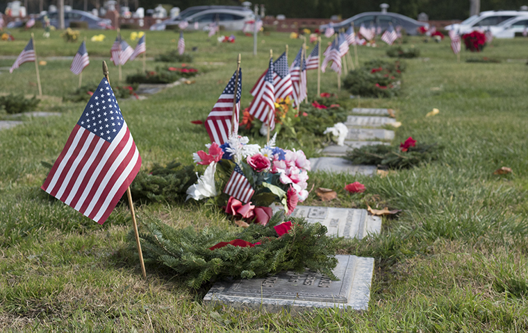 Graveyard with wreaths and American flags on tombstones.