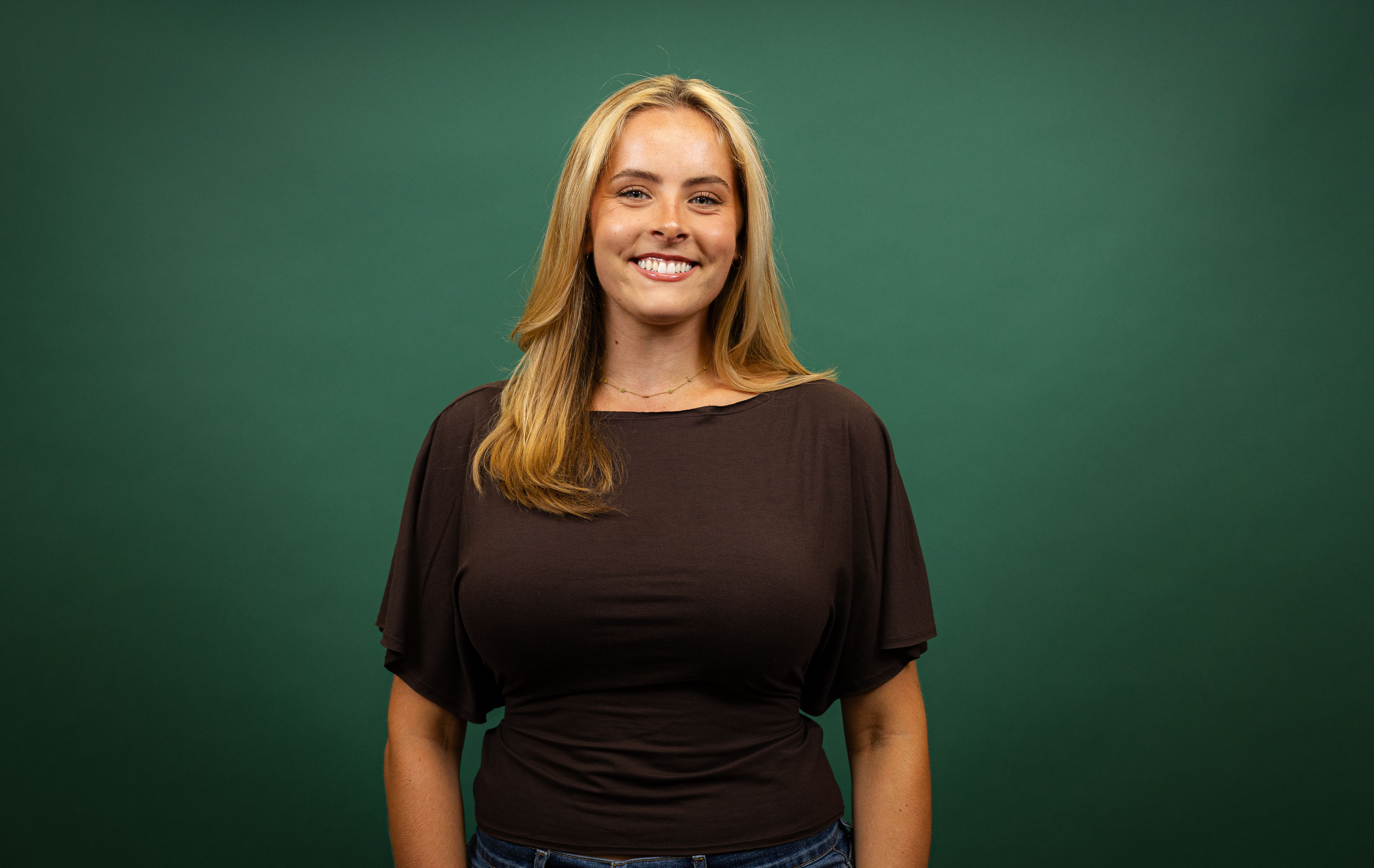 Young woman smiles in front of green backdrop.