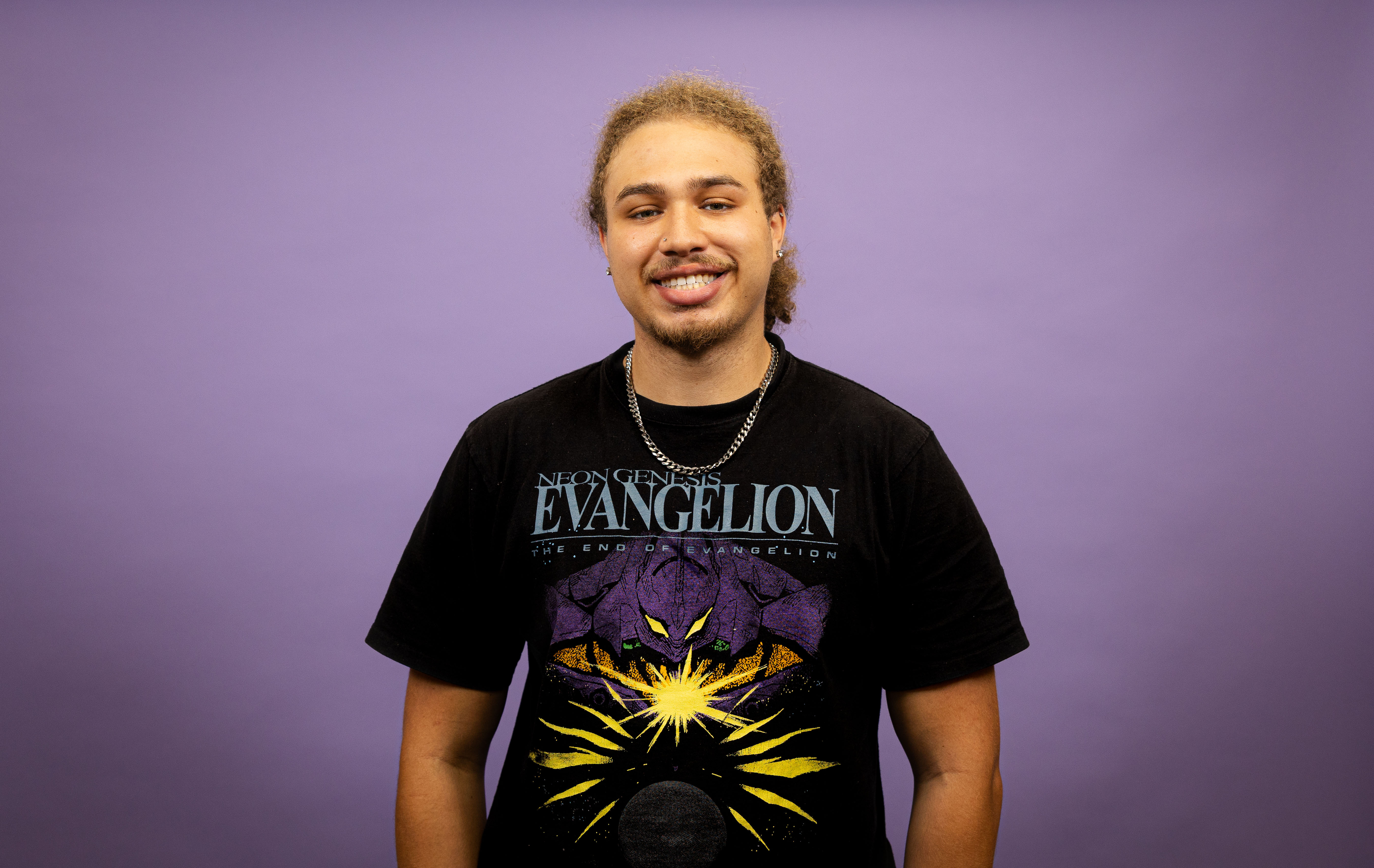 Young man smiles in front of purple backdrop.