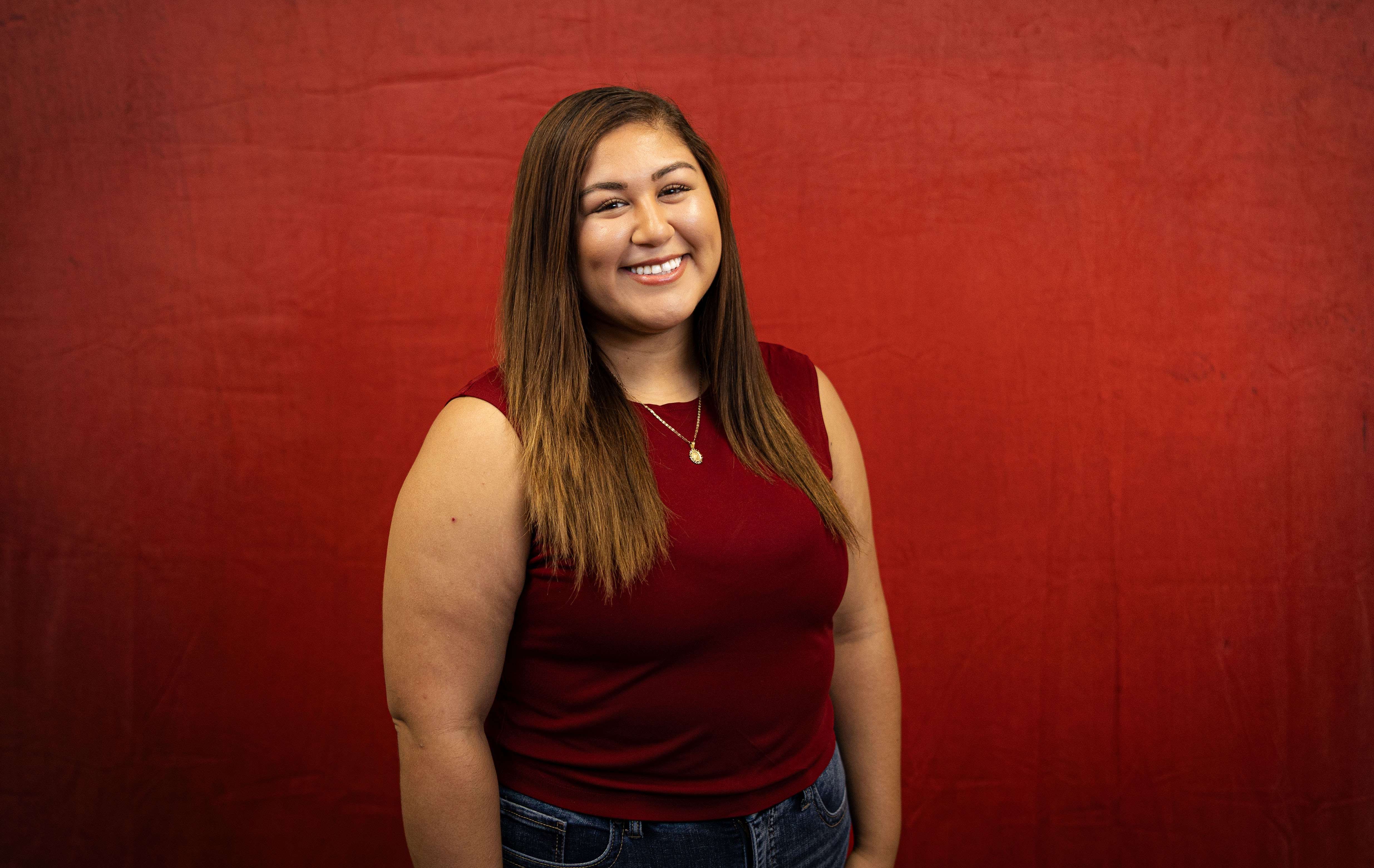 Young woman smiles in front of red backdrop.